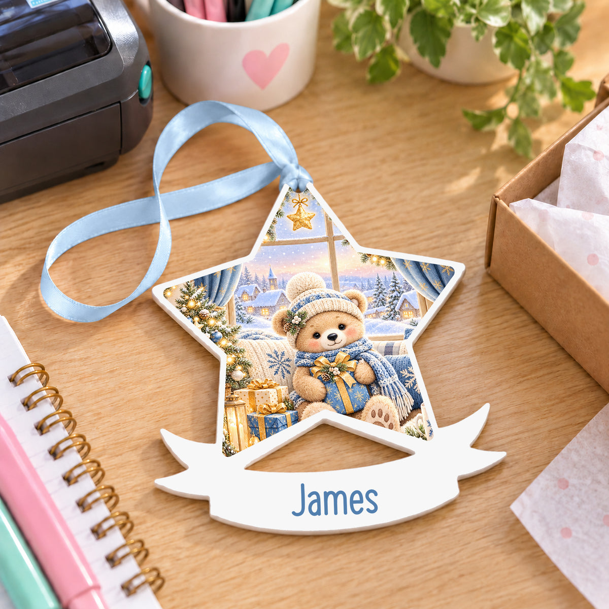 Personalised blue Christmas window white acrylic star bauble with name, 10cm Christmas decoration with ribbon, shown on a desk