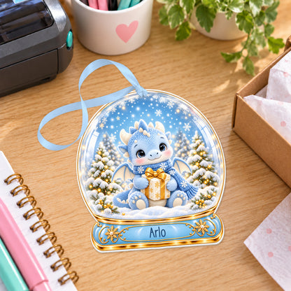 Personalised blue dragon snow globe bauble with name, white acrylic Christmas decoration with ribbon, shown on a desk
