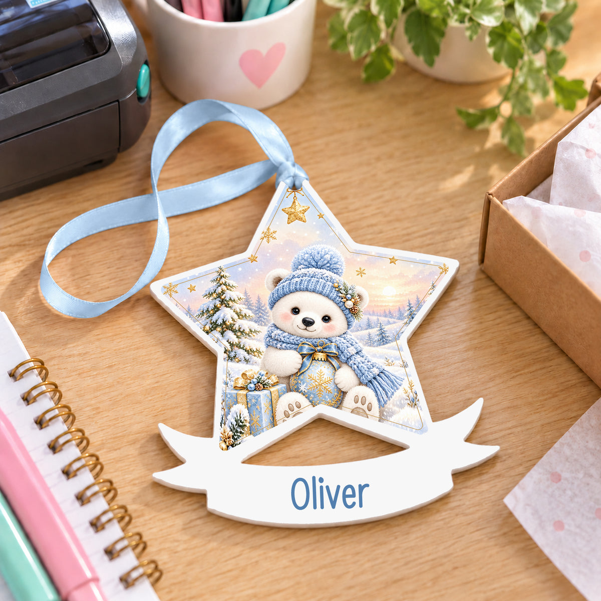 Personalised blue polar bear white acrylic star bauble with name, 10cm Christmas decoration with ribbon, shown on a desk