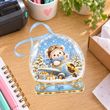 Personalised blue teddy aeroplane snow globe bauble with name, white acrylic Christmas decoration with ribbon, shown on a desk