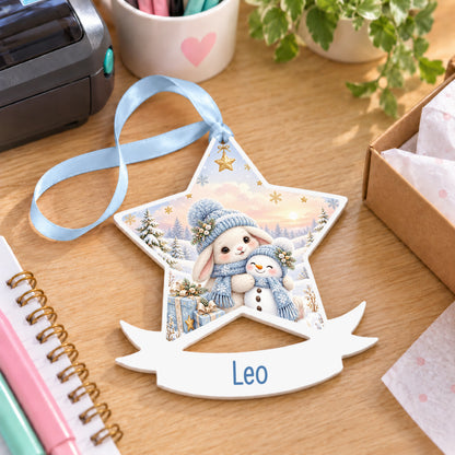 Personalised blue winter bunny white acrylic star bauble with name, 10cm Christmas decoration with ribbon, shown on a desk