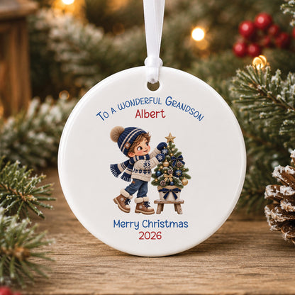 Personalised white ceramic Christmas bauble showing a little boy in a navy striped bobble hat and Nordic jumper decorating a small Christmas tree, with To a wonderful Grandson, a name and Merry Christmas 2026