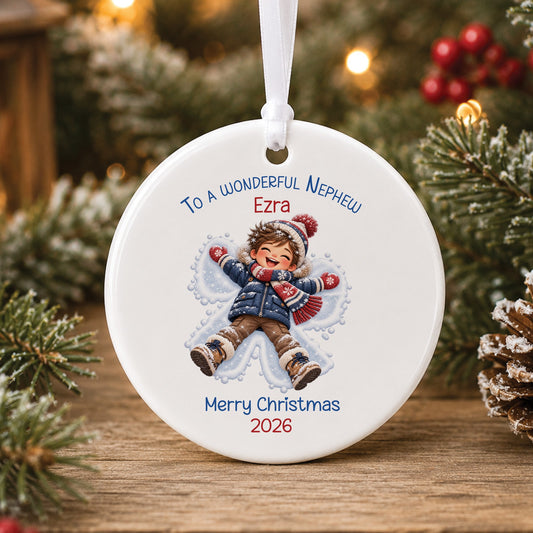 Personalised white ceramic Christmas bauble showing a laughing little boy in a navy coat and red scarf making a snow angel, with To a wonderful Grandson, a name and Merry Christmas 2026