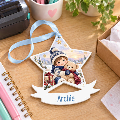 Personalised boy teddy hug white acrylic star bauble with name, 10cm Christmas decoration with ribbon, shown on a desk