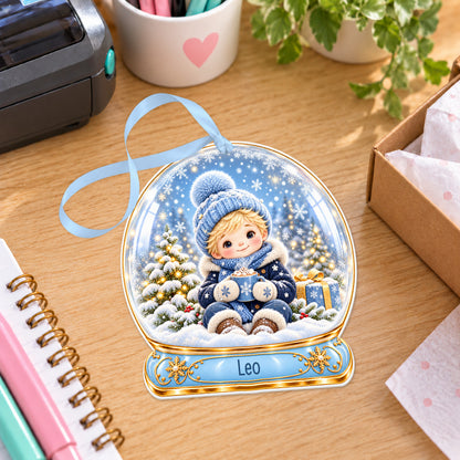Personalised boy with hot cocoa snow globe bauble with name, white acrylic Christmas decoration with ribbon, shown on a desk