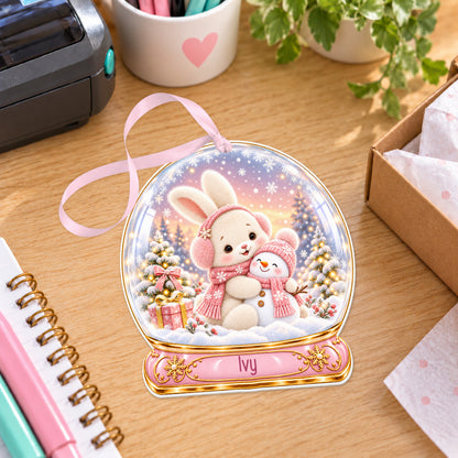 Personalised bunny and snowman snow globe bauble with name, white acrylic Christmas decoration with ribbon, shown on a desk
