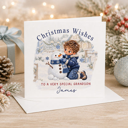 Personalised 6x6 Christmas Wishes card with a brown-haired boy in a navy puffer jacket building a snowman with a blue scarf, “To a very special grandson James”