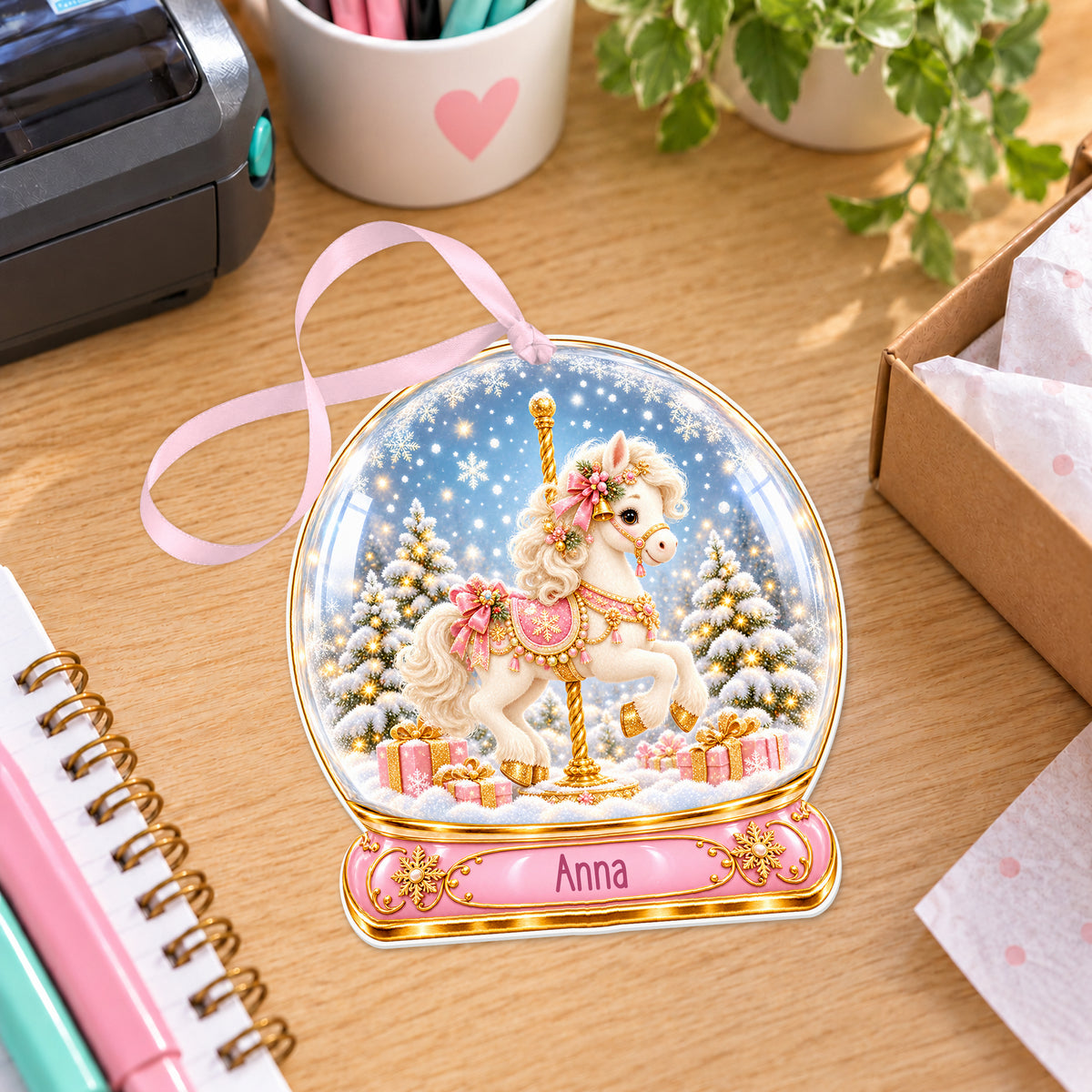 Personalised Christmas carousel snow globe bauble with name, white acrylic Christmas decoration with ribbon, shown on a desk