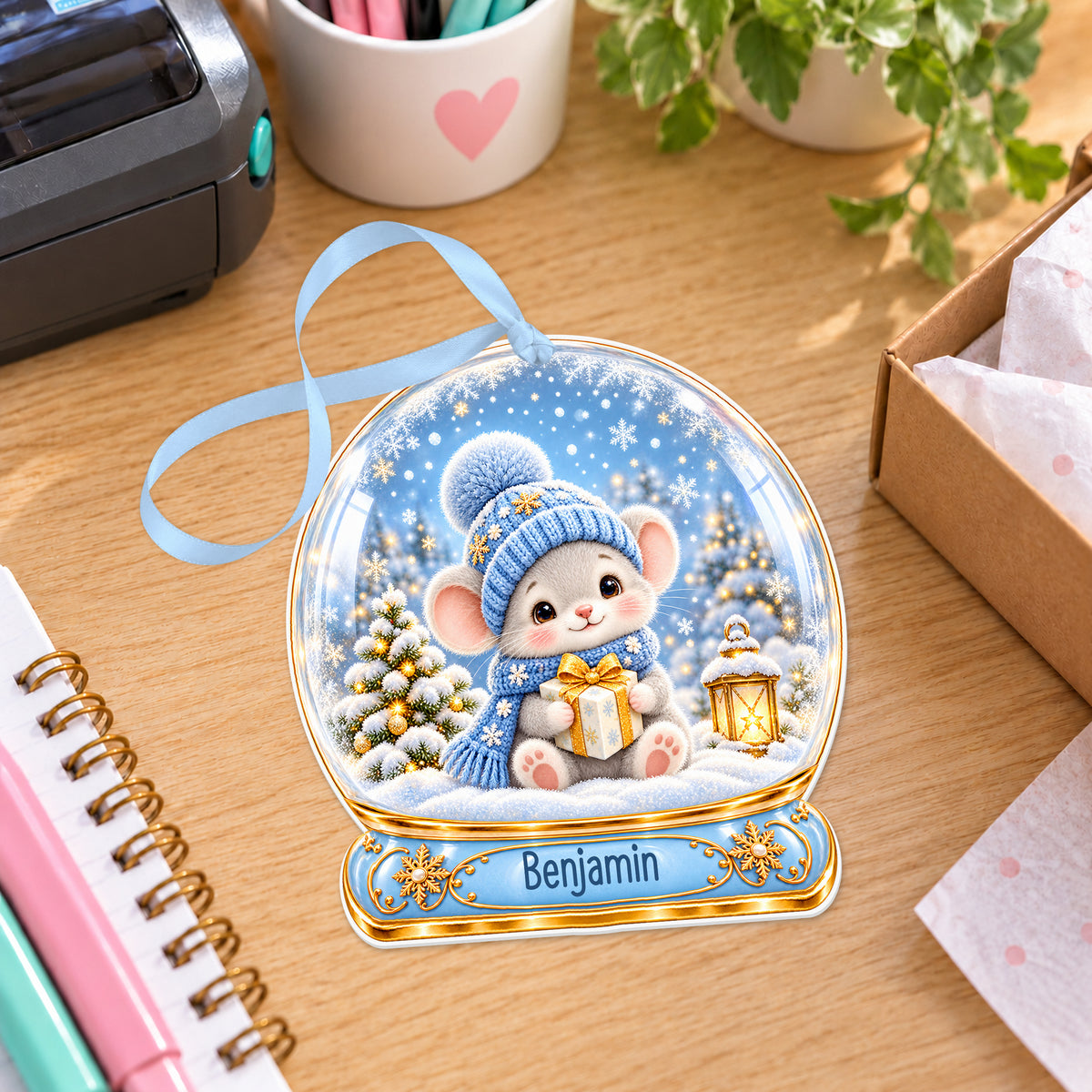 Personalised Christmas mouse snow globe bauble with name, white acrylic Christmas decoration with ribbon, shown on a desk