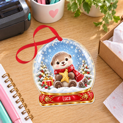 Personalised Christmas otter snow globe bauble with name, white acrylic Christmas decoration with ribbon, shown on a desk
