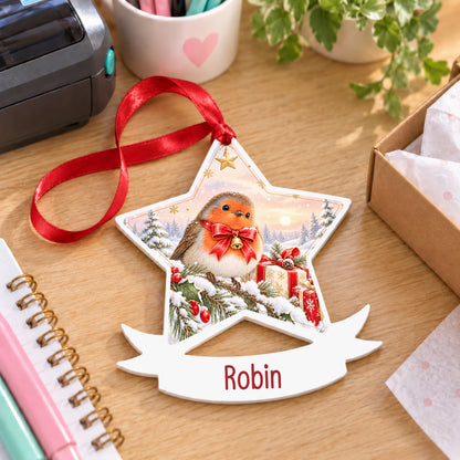Personalised Christmas robin white acrylic star bauble with name, 10cm Christmas decoration with ribbon, shown on a desk