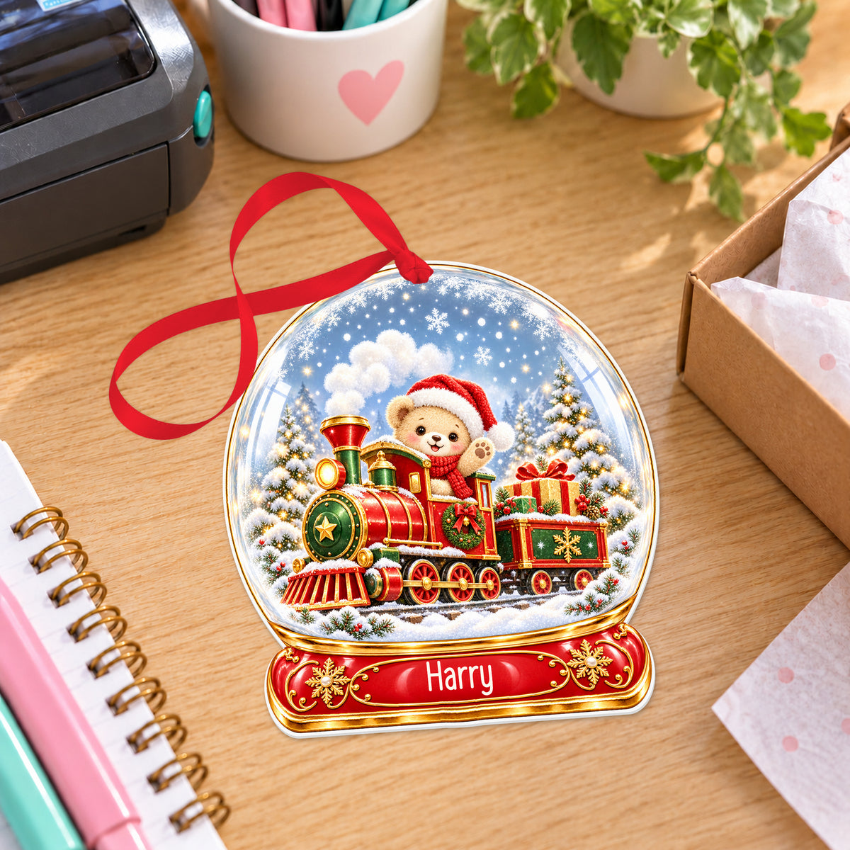 Personalised classic Christmas train snow globe bauble with name, white acrylic Christmas decoration with ribbon, shown on a desk