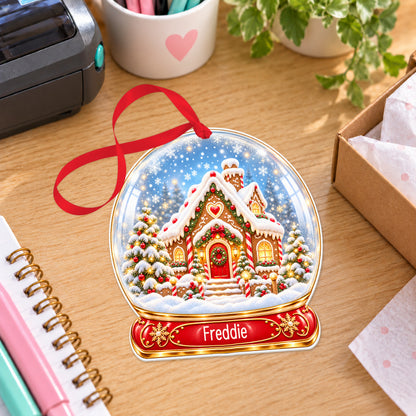 Personalised classic gingerbread house snow globe bauble with name, white acrylic Christmas decoration with ribbon, shown on a desk
