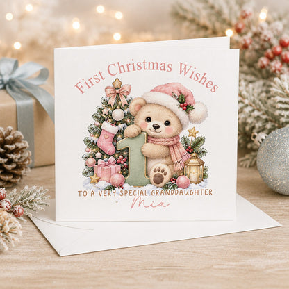 Personalised 6x6 First Christmas Wishes card with a soft teddy bear in a pink Santa hat and scarf hugging a sage green number 1 beside a Christmas tree, “To a very special granddaughter Mia”