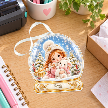 Personalised girl with bunny snow globe bauble with name, white acrylic Christmas decoration with ribbon, shown on a desk
