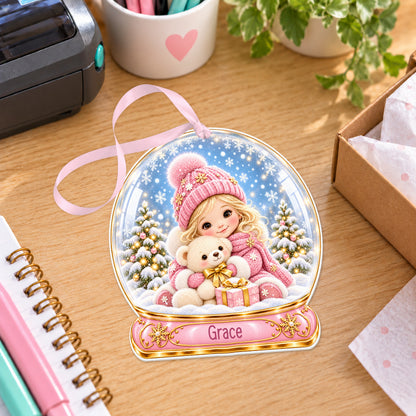 Personalised girl with teddy snow globe bauble with name, white acrylic Christmas decoration with ribbon, shown on a desk