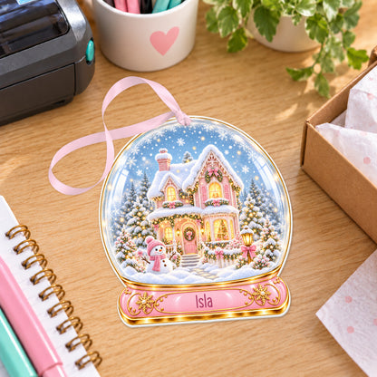 Personalised pink Christmas house snow globe bauble with name, white acrylic Christmas decoration with ribbon, shown on a desk
