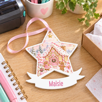 Personalised pink gingerbread cottage white acrylic star bauble with name, 10cm Christmas decoration with ribbon, shown on a desk