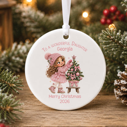 Personalised white ceramic Christmas bauble showing a little girl with long curly hair in a pink bobble hat and tutu decorating a small Christmas tree with pink baubles, with To a wonderful Niece or Daughter, a name and Merry Christmas 2026 in pink