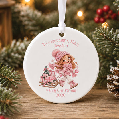 Personalised white ceramic Christmas bauble showing a little girl with long strawberry blonde hair in a pink bobble hat pulling a sledge piled with pink presents, with To a wonderful Niece or Daughter, a name and Merry Christmas 2026 in pink