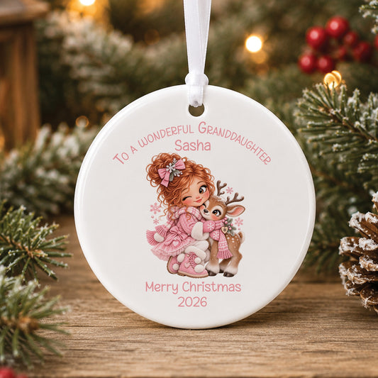 Personalised white ceramic Christmas bauble showing a little girl with red curly hair in a pink coat and bow hugging a baby reindeer in a pink scarf, with To a wonderful Granddaughter, a name and Merry Christmas 2026 in pink