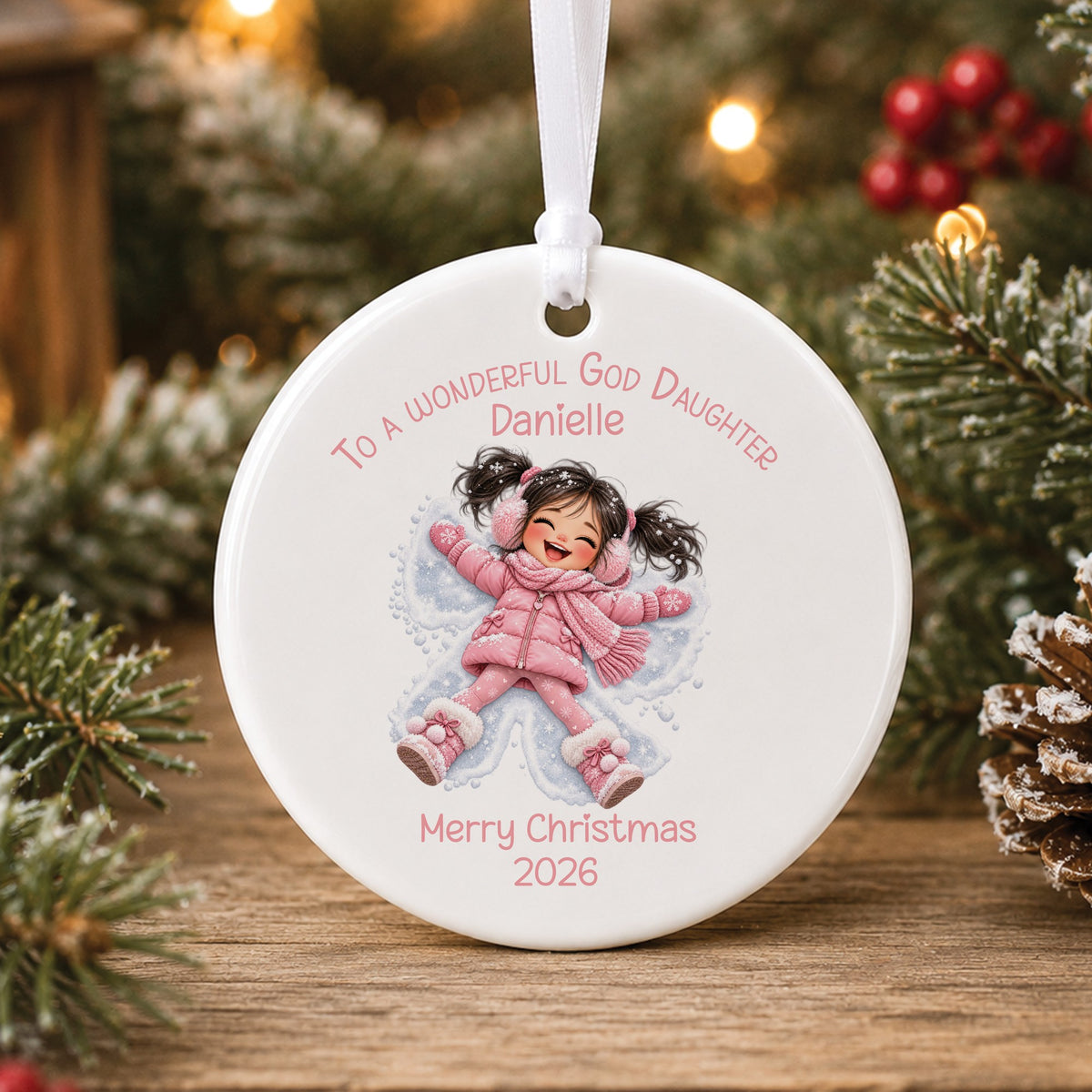 Personalised white ceramic Christmas bauble showing a laughing little girl with dark pigtails and pink earmuffs making a snow angel, with To a wonderful Granddaughter, a name and Merry Christmas 2026 in pink