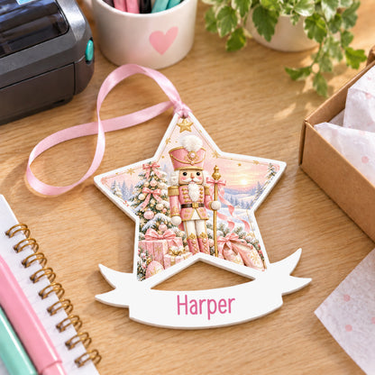 Personalised pink nutcracker white acrylic star bauble with name, 10cm Christmas decoration with ribbon, shown on a desk