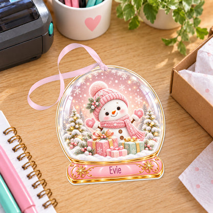 Personalised pink snowman snow globe bauble with name, white acrylic Christmas decoration with ribbon, shown on a desk