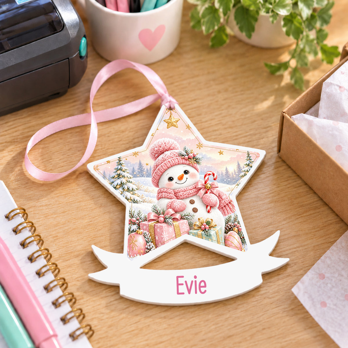 Personalised pink snowman white acrylic star bauble with name, 10cm Christmas decoration with ribbon, shown on a desk