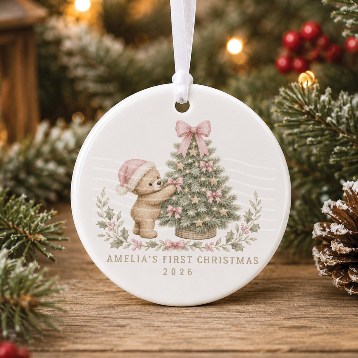 Personalised white ceramic baby’s first Christmas bauble with a teddy bear in a pink Santa hat decorating a tree with pink bows, “Amelia’s First Christmas 2026”