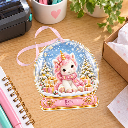 Personalised pink unicorn snow globe bauble with name, white acrylic Christmas decoration with ribbon, shown on a desk
