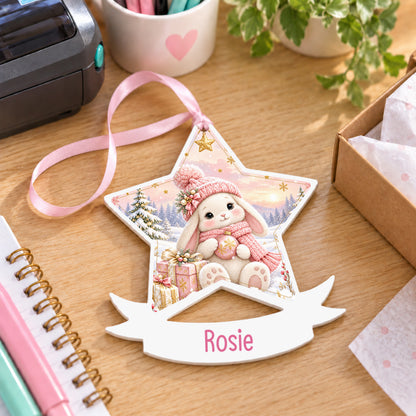 Personalised pink winter bunny white acrylic star bauble with name, 10cm Christmas decoration with ribbon, shown on a desk