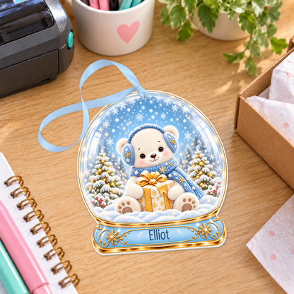 Personalised polar bear cub snow globe bauble with name, white acrylic Christmas decoration with ribbon, shown on a desk