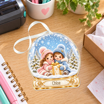 Personalised siblings with presents snow globe bauble with name, white acrylic Christmas decoration with ribbon, shown on a desk