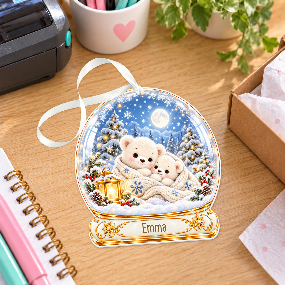 Personalised sleepy polar bears snow globe bauble with name, white acrylic Christmas decoration with ribbon, shown on a desk