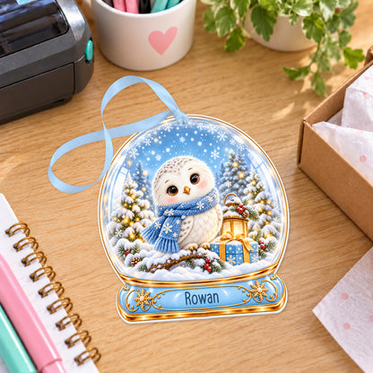 Personalised snowy owl snow globe bauble with name, white acrylic Christmas decoration with ribbon, shown on a desk
