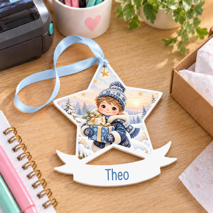 Personalised winter boy with gifts white acrylic star bauble with name, 10cm Christmas decoration with ribbon, shown on a desk