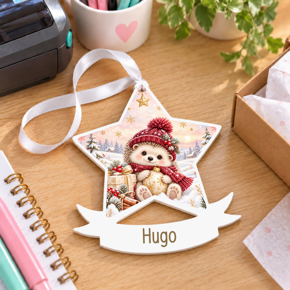Personalised winter hedgehog white acrylic star bauble with name, 10cm Christmas decoration with ribbon, shown on a desk