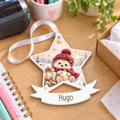 Personalised winter hedgehog white acrylic star bauble with name, 10cm Christmas decoration with ribbon, shown on a desk