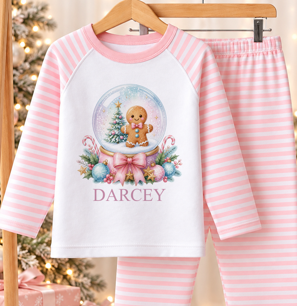 Personalised pink and white striped kids Christmas pyjamas with Gingerbread Snow Globe design and a custom name printed on the front