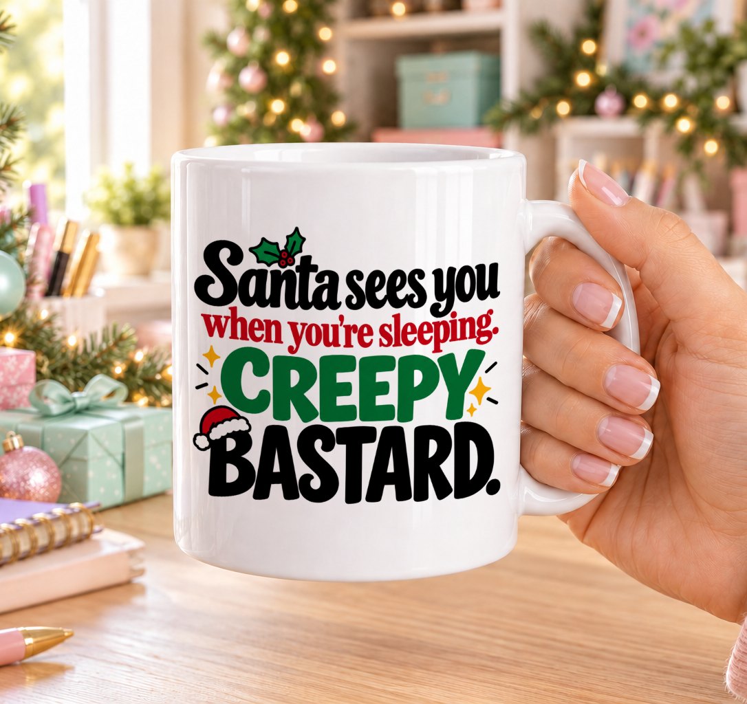 White 11oz ceramic Christmas mug printed with “Santa sees you when you’re sleeping. Creepy bastard.” in red, green and black lettering with Santa hat and holly details, held in a festive room