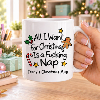 White personalised funny Christmas mug printed with “All I want for Christmas is a f*cking nap” with holly, a gingerbread man, candy cane and stars, and the line “Tracy’s Christmas Mug” underneath
