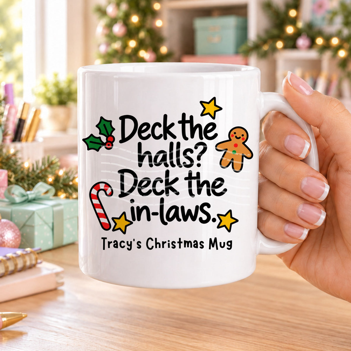 White personalised funny Christmas mug printed with “Deck the halls? Deck the in-laws.” with holly, a gingerbread man, candy cane and stars, and the line “Tracy’s Christmas Mug” underneath