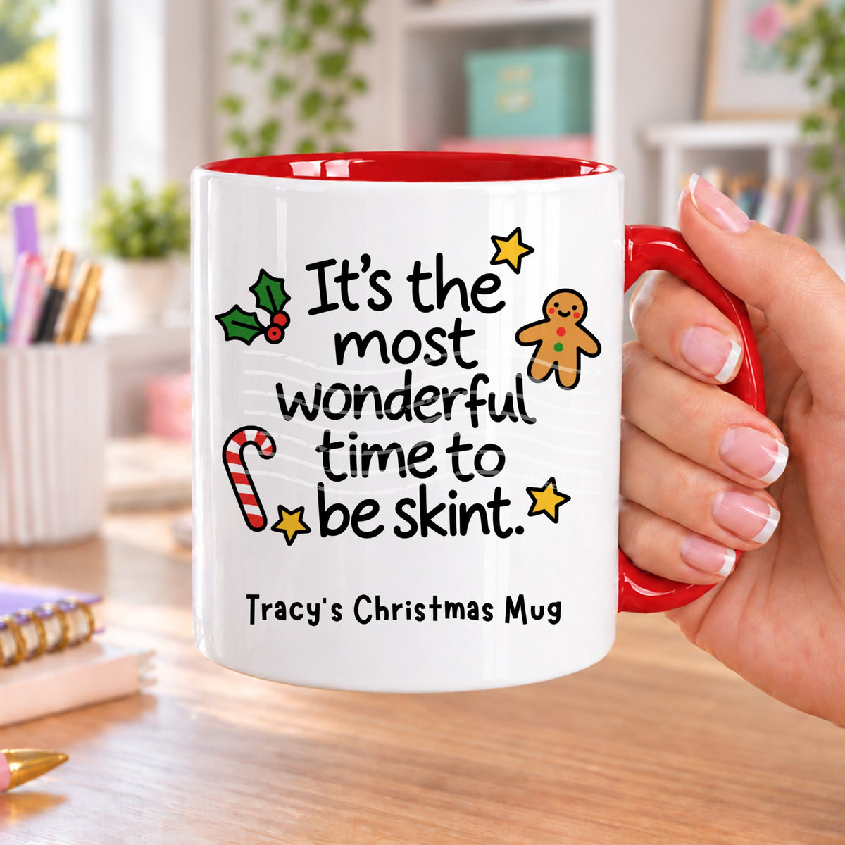 Red handled personalised funny Christmas mug printed with “It’s the most wonderful time to be skint.” with holly, a gingerbread man, candy cane and stars, and the line “Tracy’s Christmas Mug” underneath
