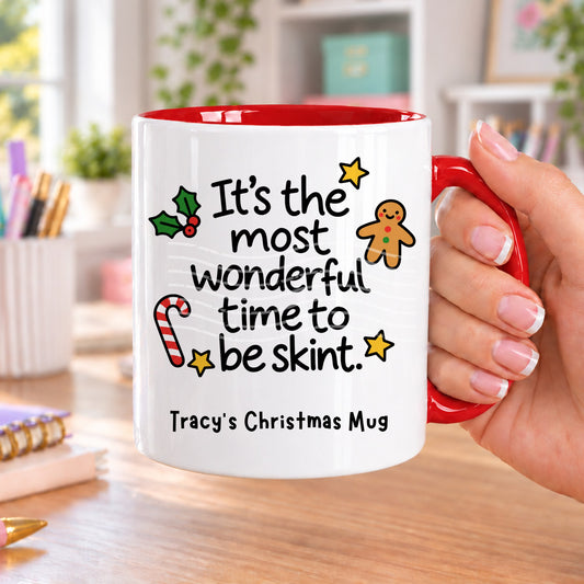 Red handled personalised funny Christmas mug printed with “It’s the most wonderful time to be skint.” with holly, a gingerbread man, candy cane and stars, and the line “Tracy’s Christmas Mug” underneath