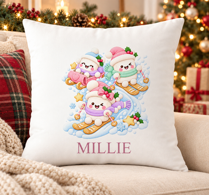 Personalised white Christmas cushion with three marshmallows skiing in bobble hats and a name printed underneath, on a festive sofa