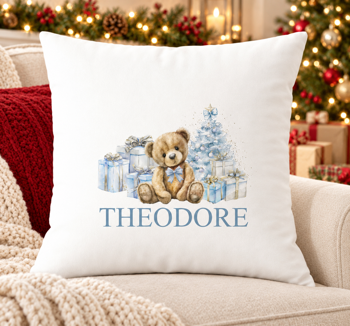 Personalised white Christmas cushion with a teddy bear with pale blue presents and a frosty tree and a name printed underneath, on a festive sofa