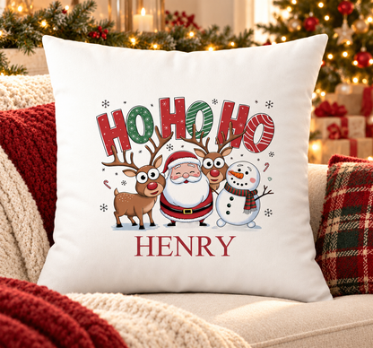 Personalised white Christmas cushion with a 'Ho Ho Ho' design with Santa, reindeer and a snowman and a name printed underneath, on a festive sofa