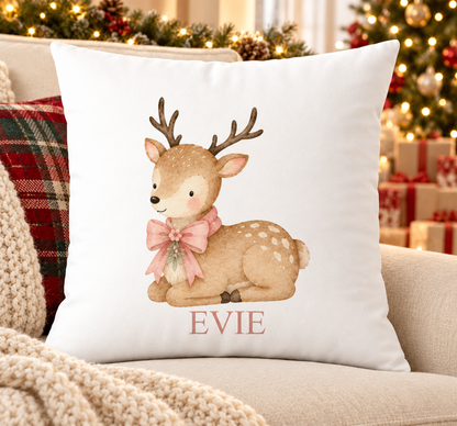 Personalised white Christmas cushion with a resting baby deer with a pink bow and a name printed underneath, on a festive sofa