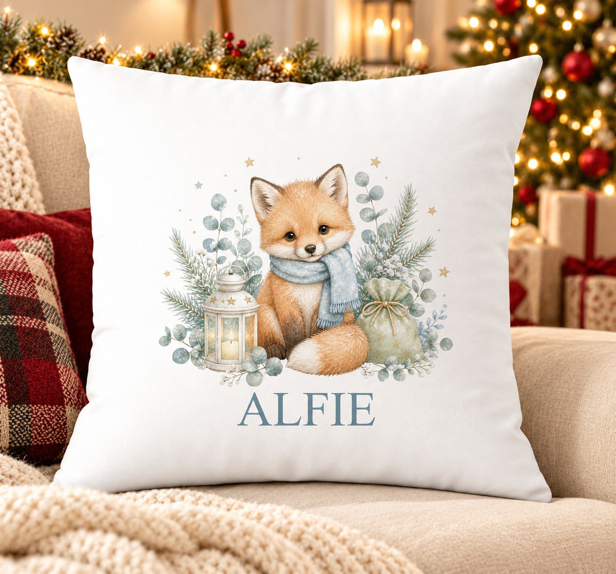 Personalised white Christmas cushion with a woodland fox in a blue scarf beside a lantern and a name printed underneath, on a festive sofa
